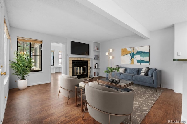 living area featuring a textured ceiling, built in shelves, a fireplace, beam ceiling, and dark wood-style floors