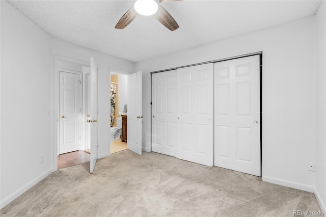 unfurnished bedroom featuring a closet, light colored carpet, ceiling fan, ensuite bath, and baseboards