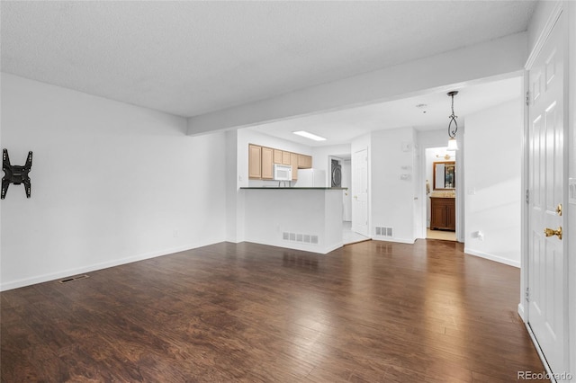 unfurnished living room featuring baseboards, a textured ceiling, visible vents, and dark wood-type flooring