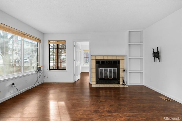 unfurnished living room with dark wood-type flooring, visible vents, a textured ceiling, and built in shelves