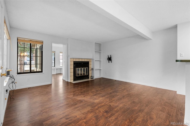 unfurnished living room with beam ceiling, dark wood-style flooring, visible vents, a tile fireplace, and baseboards