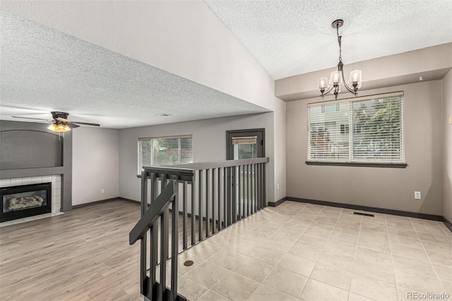 10172 Woodrose Ln, Highlands Ranch, CO 80129 - spare room featuring a textured ceiling, a fireplace, a chandelier, ceiling fan, and light wood-style flooring