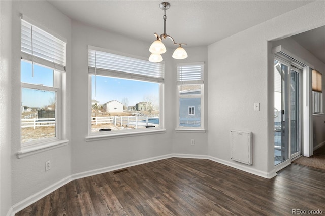 unfurnished dining area featuring an inviting chandelier, plenty of natural light, and dark hardwood / wood-style floors