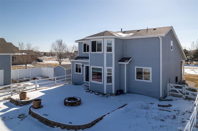 snow covered back of property with a storage shed and an outdoor fire pit