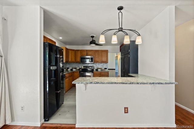 4627 S Norfolk Way, Aurora, CO 80015 - kitchen featuring appliances with stainless steel finishes, a peninsula, a ceiling fan, brown cabinets, and tasteful backsplash
