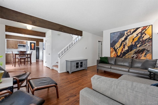 living room with wood finished floors, a textured ceiling, stairway, baseboards, and beamed ceiling