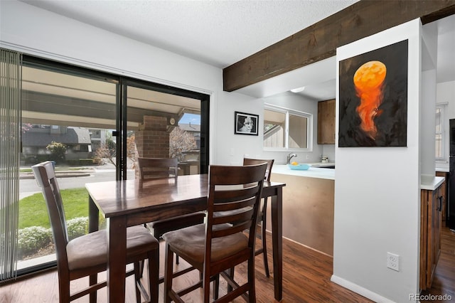 dining area featuring baseboards, dark wood finished floors, beam ceiling, and a textured ceiling