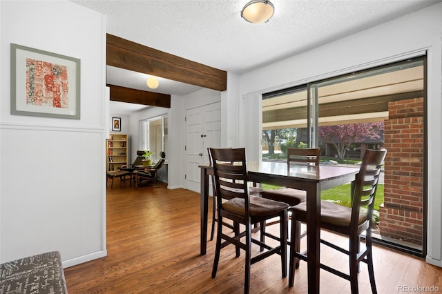 dining space featuring a textured ceiling, wood finished floors, and beam ceiling