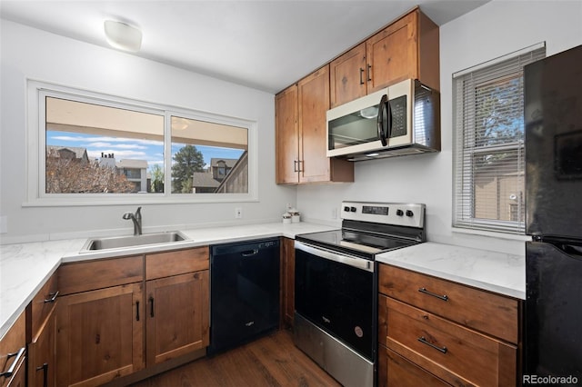kitchen with a sink, brown cabinets, black appliances, light stone counters, and dark wood-style flooring
