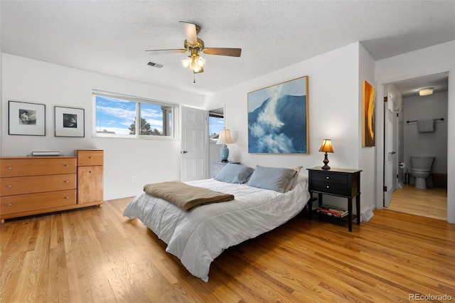 bedroom featuring a textured ceiling, visible vents, a ceiling fan, connected bathroom, and light wood-style floors