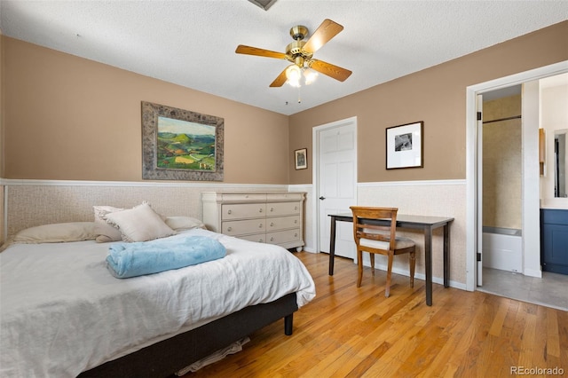 bedroom with light wood-style flooring, a textured ceiling, and a wainscoted wall