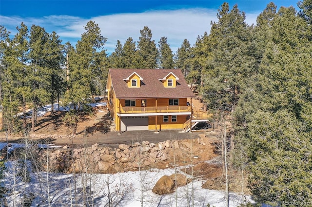 view of front of property featuring a view of trees, a garage, and a wooden deck