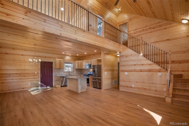 kitchen featuring wooden walls, open floor plan, wood ceiling, light wood-type flooring, and appliances with stainless steel finishes