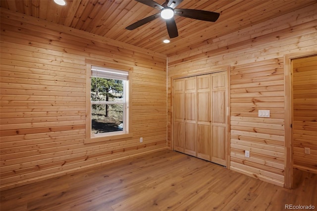 unfurnished bedroom featuring wooden walls, ceiling fan, wood ceiling, light wood-type flooring, and two closets