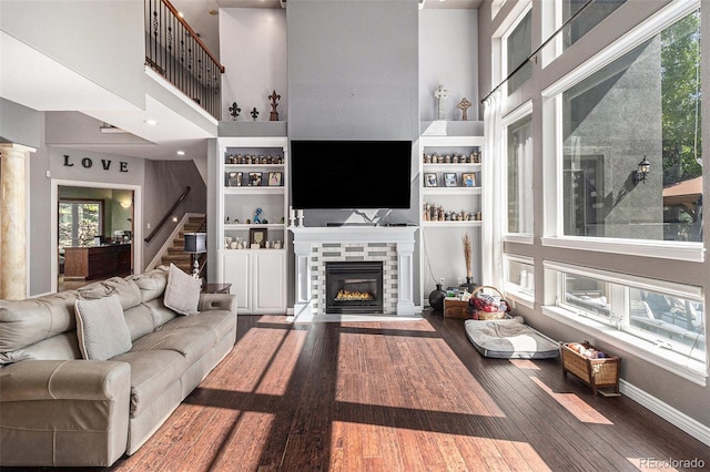 6940 Saddleback Ave, Firestone, CO 80504 - living room featuring a towering ceiling, a glass covered fireplace, wood finished floors, plenty of natural light, and stairs