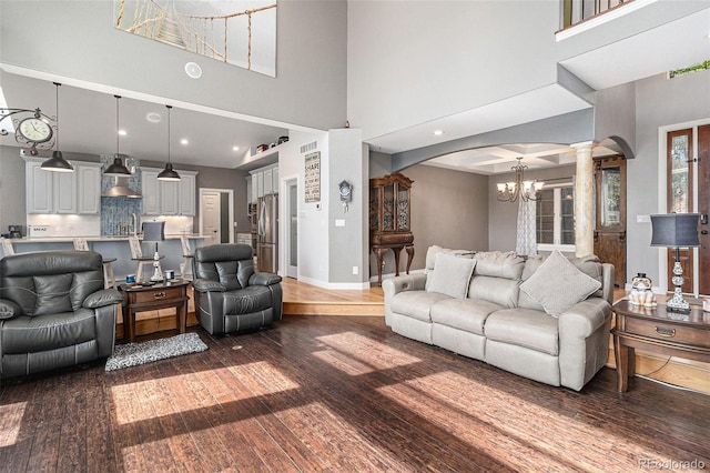 6940 Saddleback Ave, Firestone, CO 80504 - living room featuring arched walkways, ornate columns, dark wood finished floors, a high ceiling, and a chandelier
