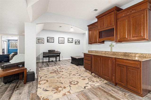 6940 Saddleback Ave, Firestone, CO 80504 - kitchen featuring light wood-style floors, arched walkways, light stone counters, and brown cabinetry
