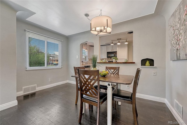 dining room with arched walkways, dark wood-style flooring, and baseboards