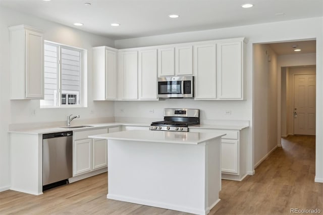 kitchen with appliances with stainless steel finishes, sink, white cabinets, a center island, and light hardwood / wood-style floors