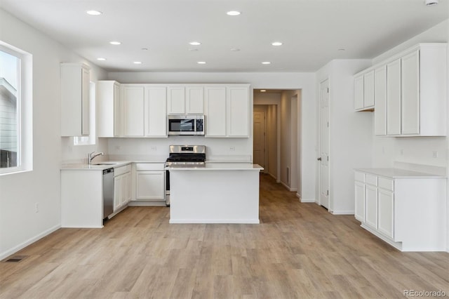 kitchen featuring sink, light hardwood / wood-style flooring, appliances with stainless steel finishes, white cabinetry, and a kitchen island