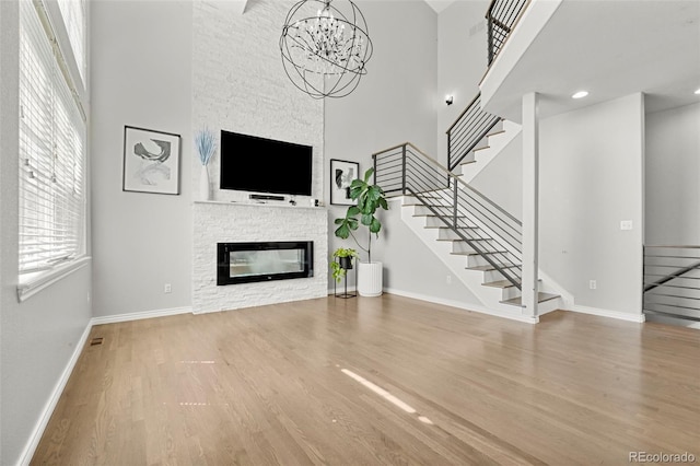 3026 S Waco Ct, Aurora, CO 80013 - unfurnished living room with a high ceiling, wood finished floors, stairs, a stone fireplace, and a chandelier