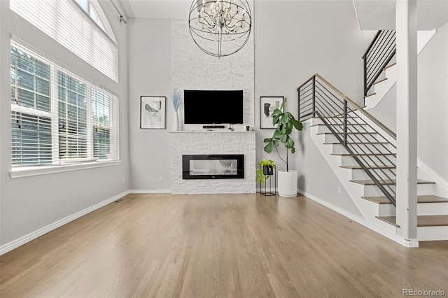 3026 S Waco Ct, Aurora, CO 80013 - unfurnished living room with a high ceiling, a stone fireplace, wood finished floors, stairway, and a chandelier