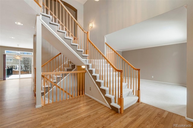 stairs with a high ceiling, baseboards, and wood finished floors