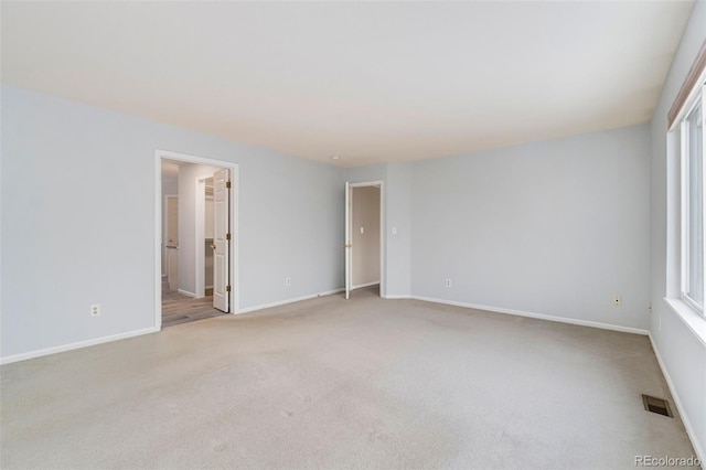 empty room featuring baseboards, visible vents, and light colored carpet