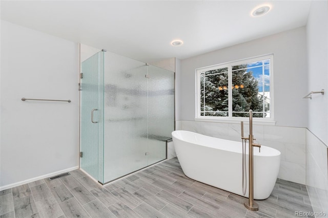 full bath featuring a stall shower, wood finish floors, a freestanding tub, and visible vents