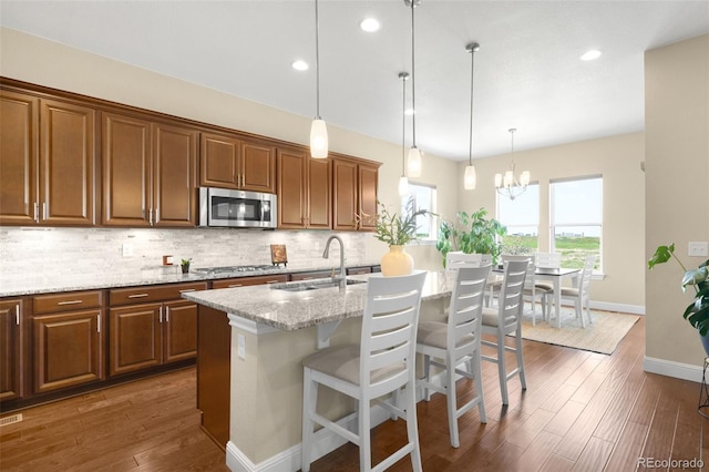 15779 W 83rd Pl, Arvada, CO 80007 - kitchen featuring stainless steel appliances, a sink, decorative backsplash, light stone counters, and brown cabinetry