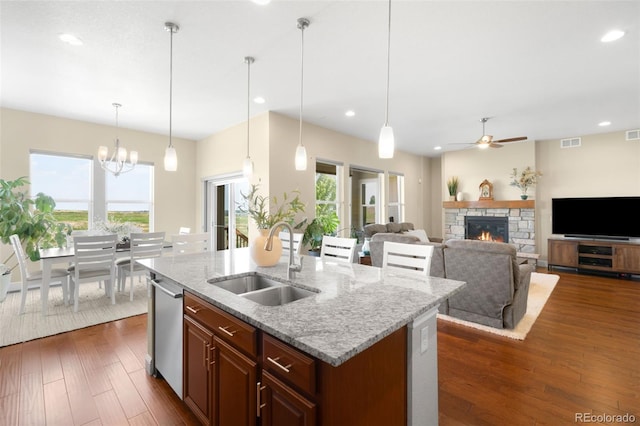 15779 W 83rd Pl, Arvada, CO 80007 - kitchen featuring a sink, a ceiling fan, a stone fireplace, a kitchen island with sink, and dark wood-style floors
