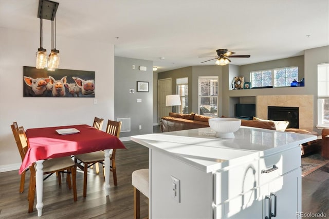 kitchen with visible vents, open floor plan, hanging light fixtures, a tiled fireplace, and dark wood finished floors