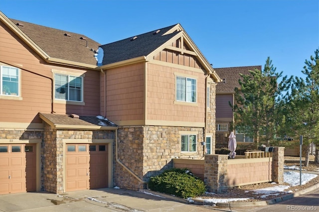 view of front of house featuring a garage, stone siding, a shingled roof, and board and batten siding