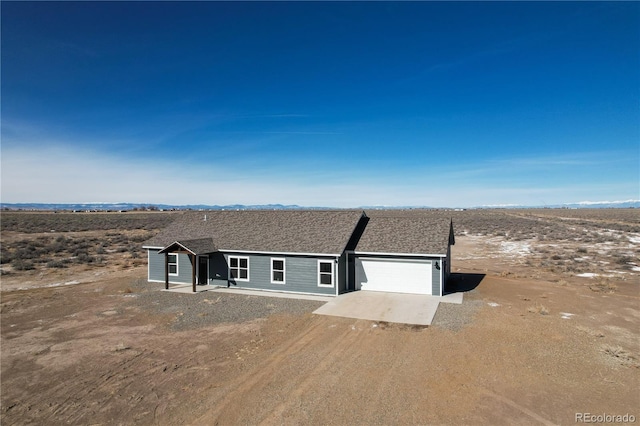 view of front facade with dirt driveway, a shingled roof, and an attached garage