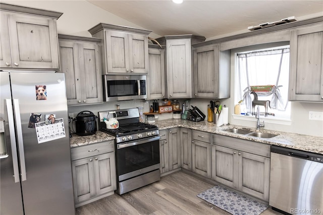 kitchen with light wood-style flooring, appliances with stainless steel finishes, light stone countertops, vaulted ceiling, and a sink