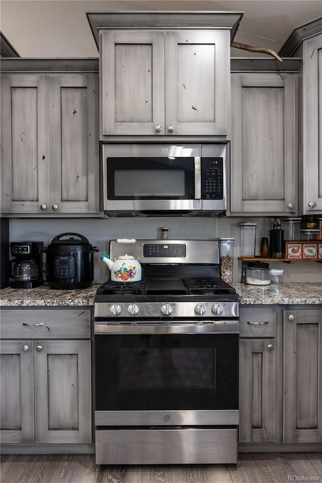 kitchen featuring stainless steel appliances, light stone counters, wood finished floors, and gray cabinetry