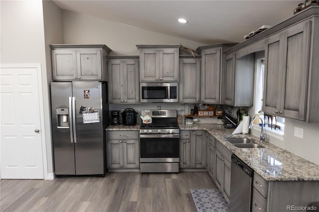 kitchen with light stone counters, dark wood-style floors, appliances with stainless steel finishes, vaulted ceiling, and a sink