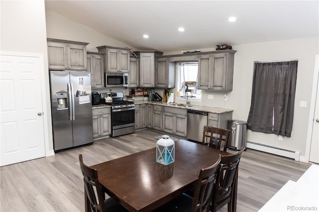 kitchen featuring a baseboard radiator, light wood-style flooring, vaulted ceiling, stainless steel appliances, and a sink