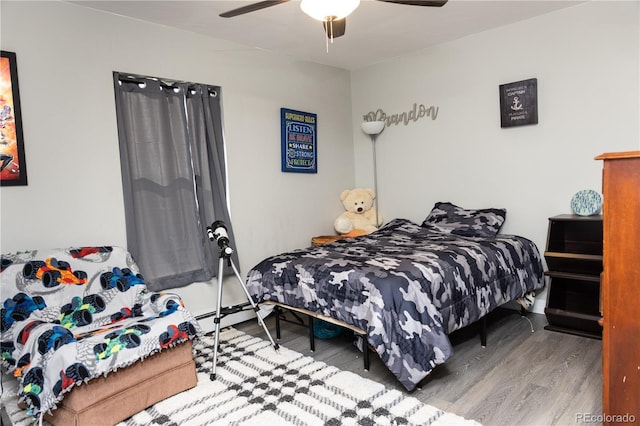 bedroom with a ceiling fan, baseboard heating, and wood finished floors