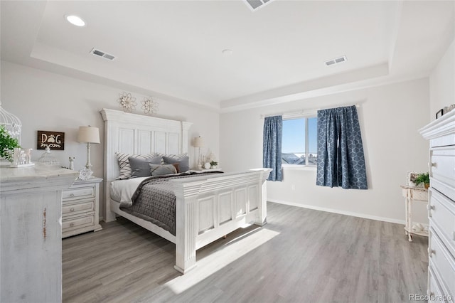 bedroom with light hardwood / wood-style flooring and a tray ceiling