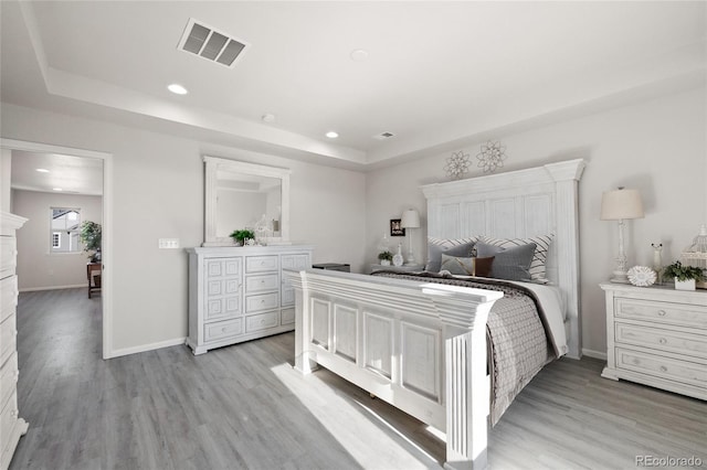 bedroom with a raised ceiling and light wood-type flooring