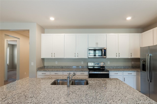 kitchen with stainless steel appliances, white cabinets, light stone counters, and sink