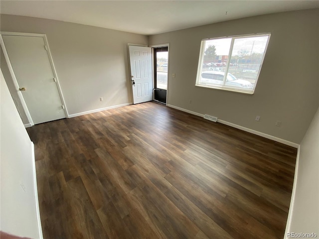 spare room featuring visible vents, a healthy amount of sunlight, baseboards, and dark wood-style flooring