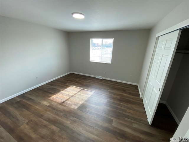 unfurnished bedroom with dark wood-type flooring, visible vents, baseboards, and a closet
