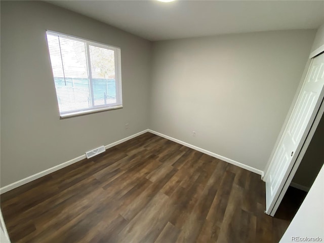 unfurnished bedroom with a closet, visible vents, dark wood-type flooring, and baseboards