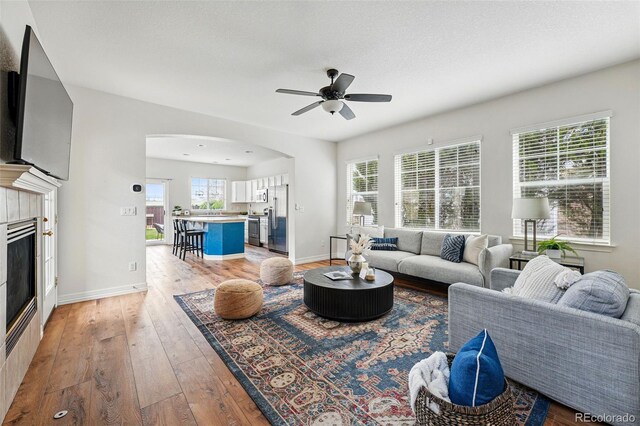 14025 Blue River Trl, Broomfield, CO 80023 - living room featuring arched walkways, light wood-style floors, ceiling fan, a fireplace, and baseboards
