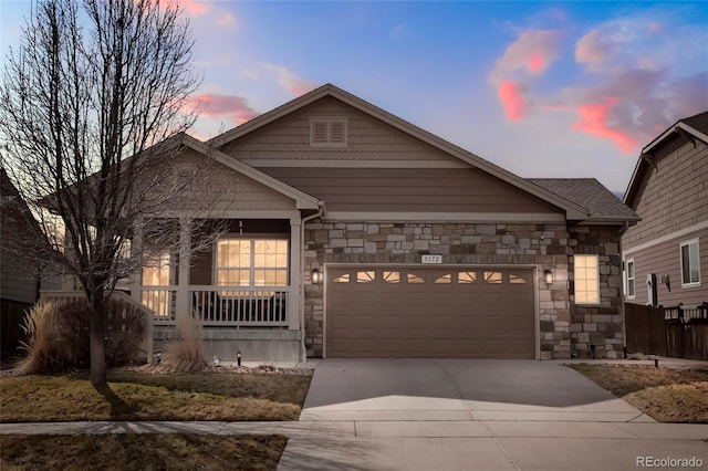 view of front of home with stone siding, driveway, a porch, and an attached garage