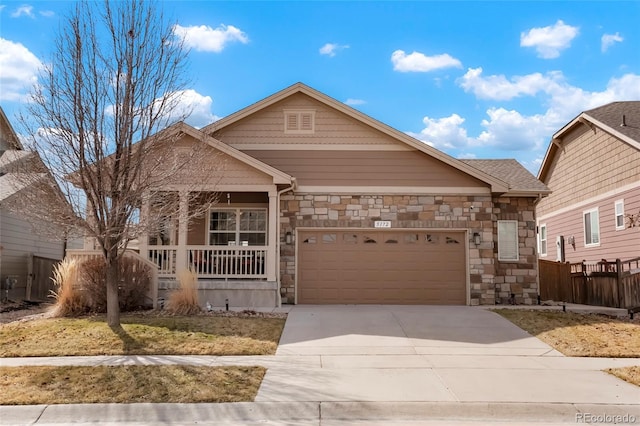 view of front of property featuring stone siding, covered porch, driveway, and a garage