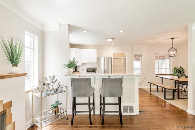 kitchen with a kitchen bar, kitchen peninsula, stainless steel appliances, pendant lighting, and white cabinets