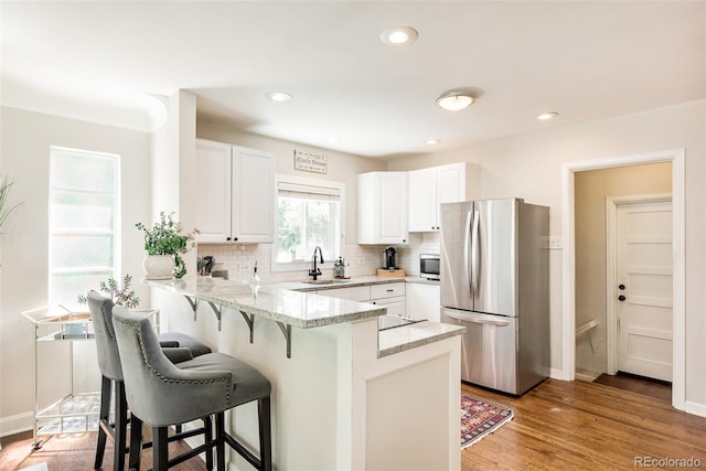 kitchen with white cabinets, sink, light wood-type flooring, kitchen peninsula, and stainless steel appliances